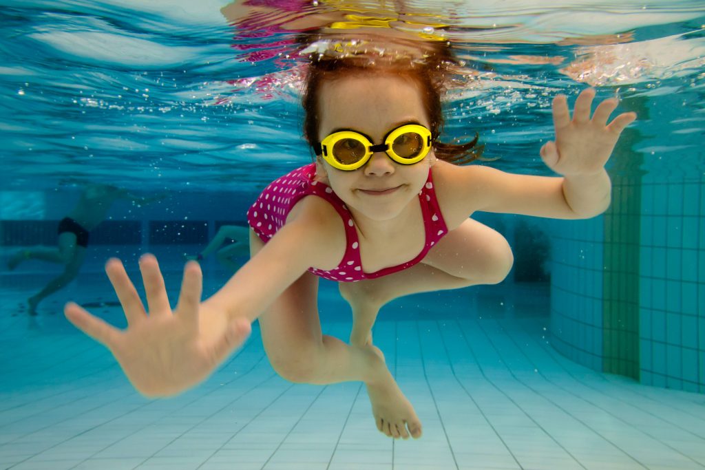 a little girl wearing water goggles and swimming underwater in a pool