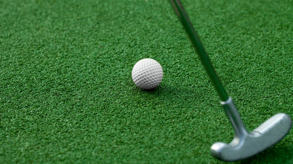 Un palo de golf a punto de golpear la pelota para meterla en el hoyo 