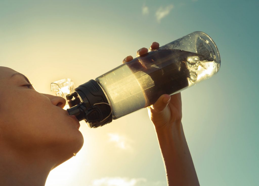 a woman drinking from a water bottle out in the hot sun