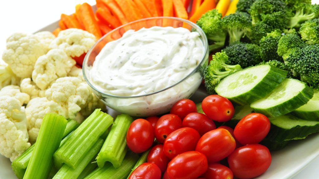 Un plato lleno de verduras frescas, como zanahorias, tomates, pepinos, brócoli y coliflor