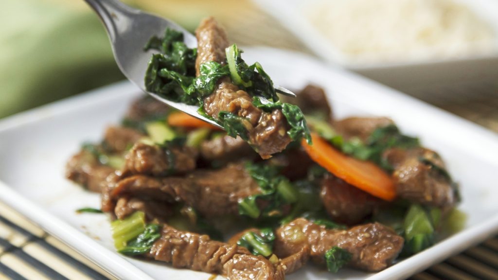 Brown-sugared pork tenderloin stir-fry on a plate with someone holding a fork