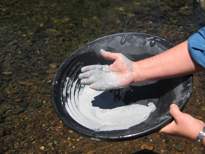 a person holding a pottery bowl near a river with blue clay and the person holding some of the clay in his or her hand