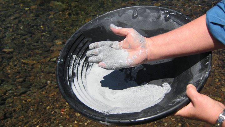Una persona sostiene un tazón de alfarería cerca de un río con arcilla blanca y tiene en la mano un poco de la arcilla 