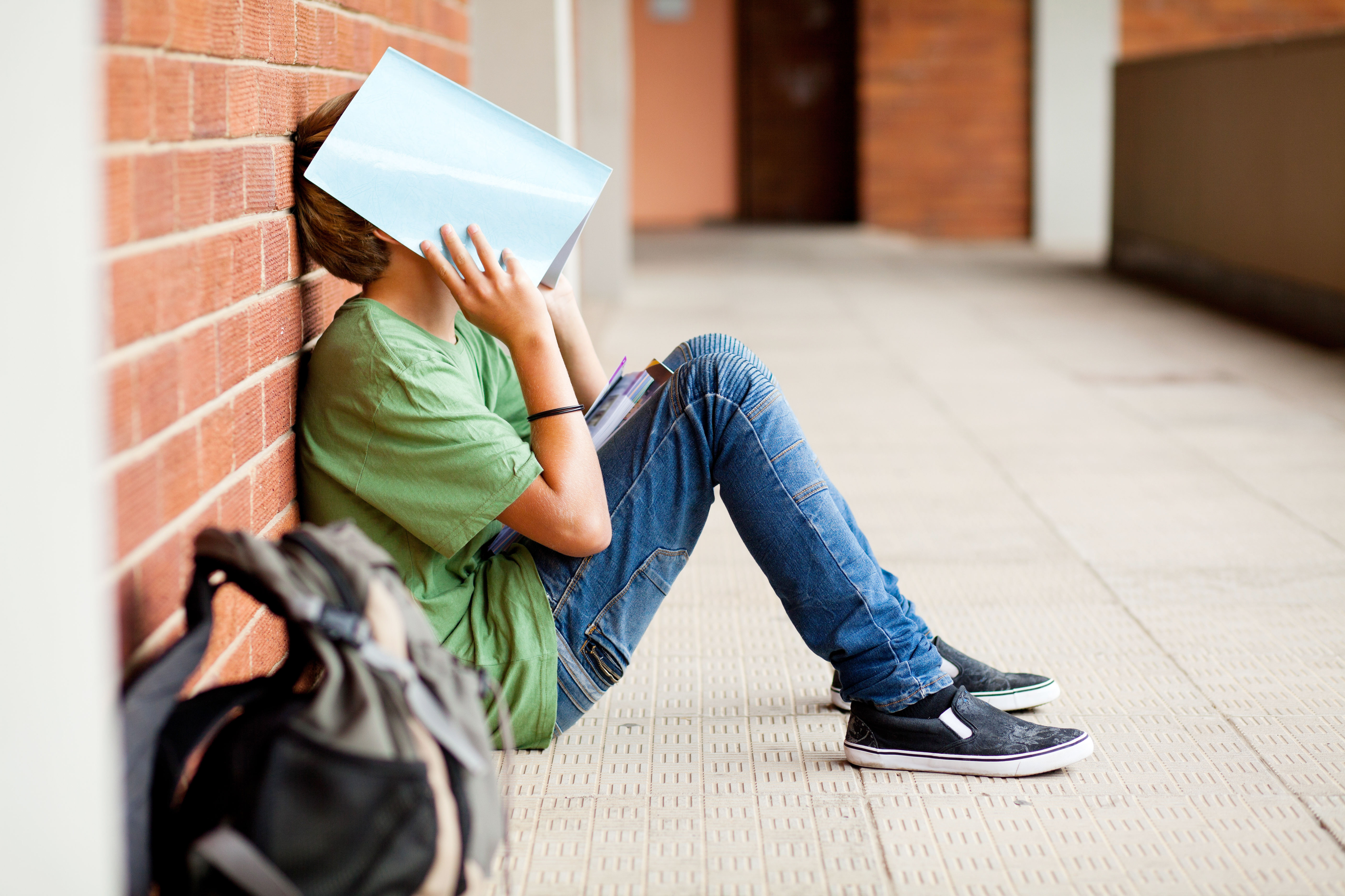 a tired student sitting on the ground using school book to cover his face, maybe stressed, anxious or frustrated
