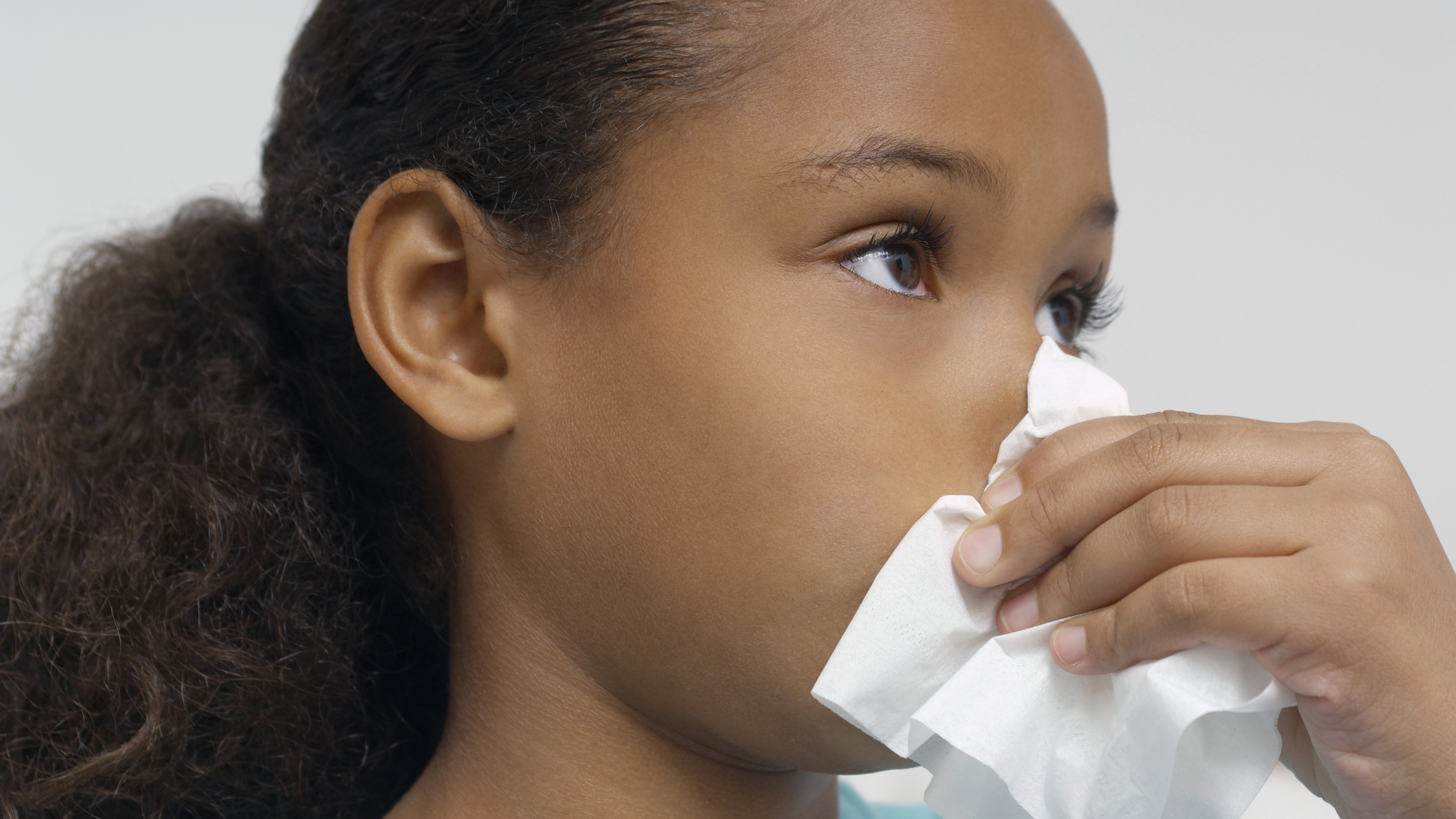 a young girl blowing her nose, perhaps sick with a cold or allergies