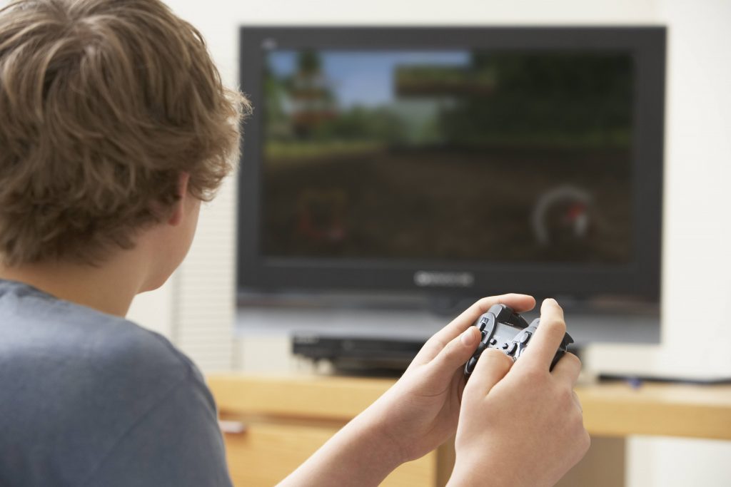 a young adolescent or teenage boy with a video game controller and looking at a television screen