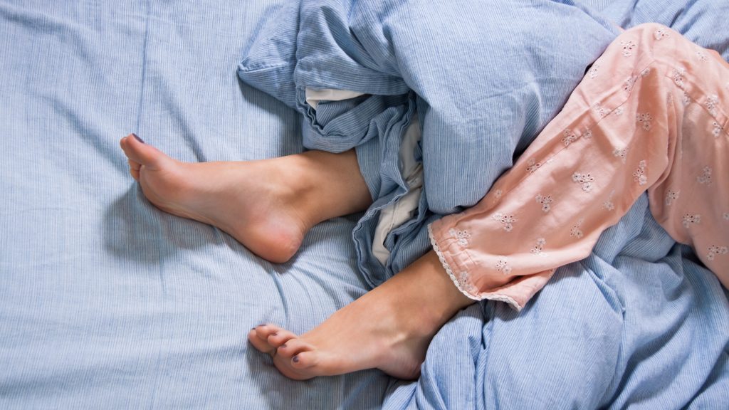 Foto de unas piernas femeninas enredadas en las sábanas y las cobijas de la cama