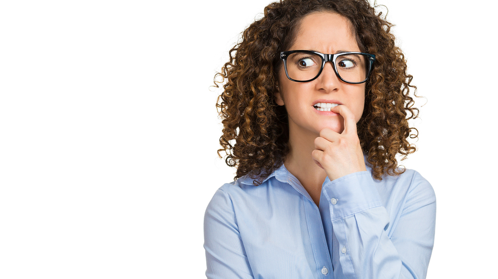 a close-up of a young woman biting her fingernail and looking anxious or embarrassed