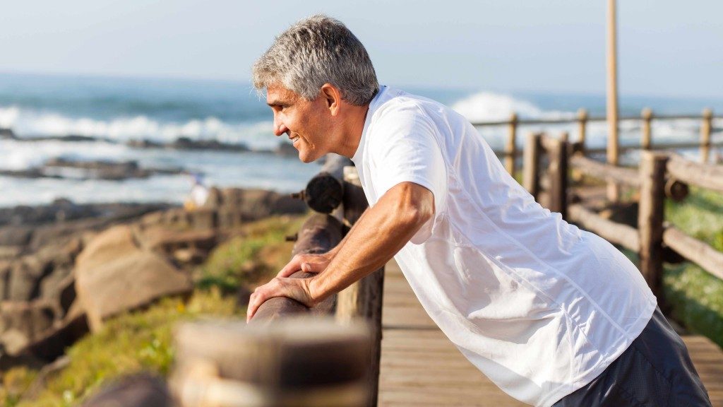 Un hombre de mediana edad hace ejercicio y se estira cerca del mar