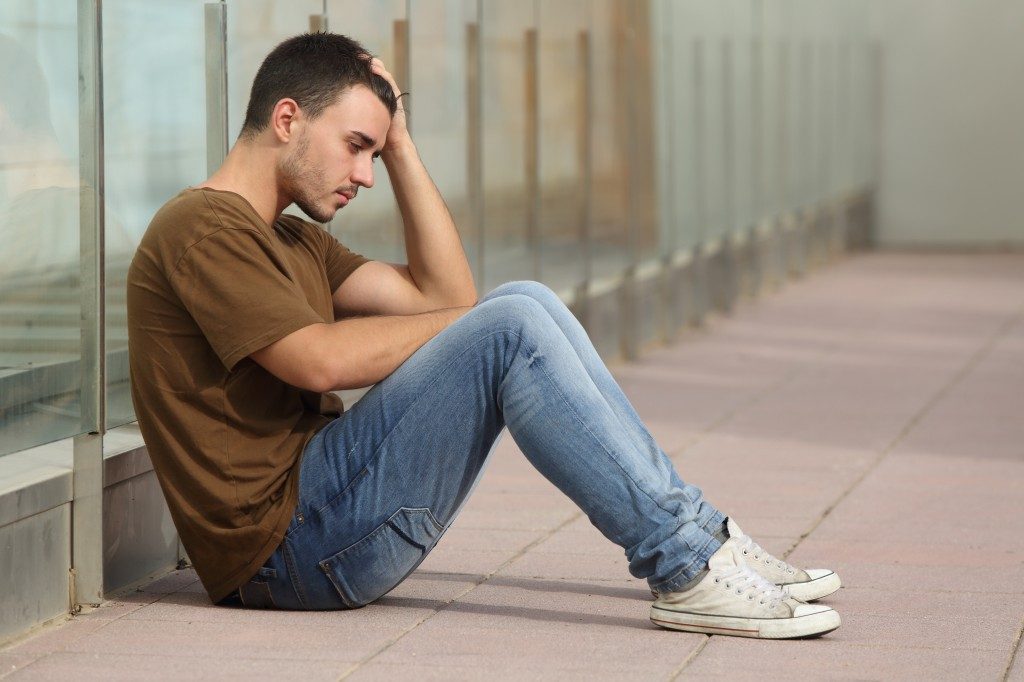 a young man, teenager, sitting on the ground leaning head on his hand looking sad, depressed, or worried