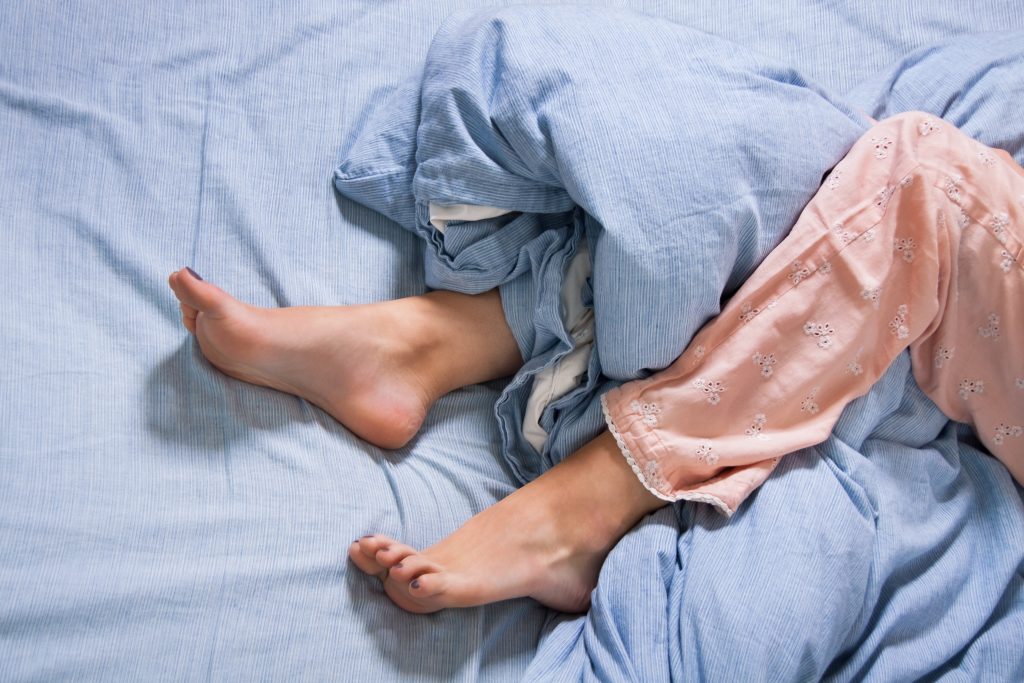a close-up of a woman's lower legs and feet in a bed, sticking out of and tangled in the sheet and blanket