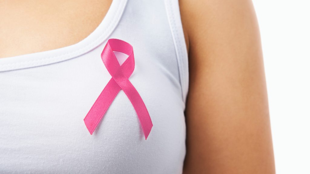 a close up of woman wearing a pink ribbon for breast cancer awareness on her white t-shirt