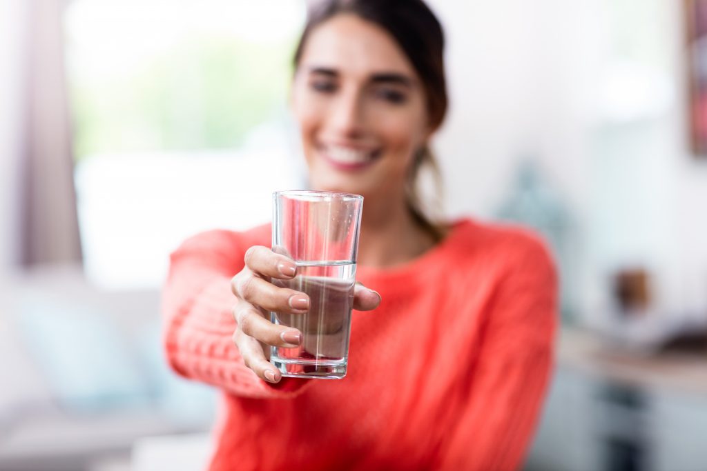 a smiling woman holding out a glass of water