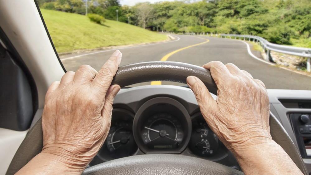 Imagen del volante y de las manos de una persona anciana que conduce un vehículo lentamente por la carretera