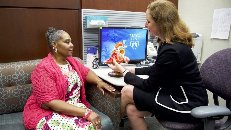 a female cardiologist talking with a woman patient in an exam room about heart disease using a model of a heart