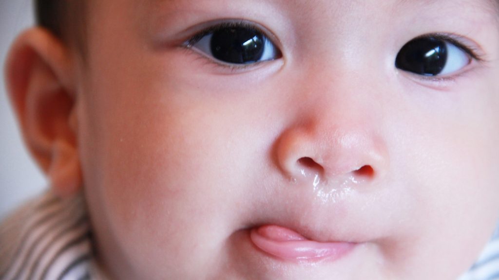 closeup of a sick baby with a flu bug, allergies or a cold with the sniffles and a runny nose