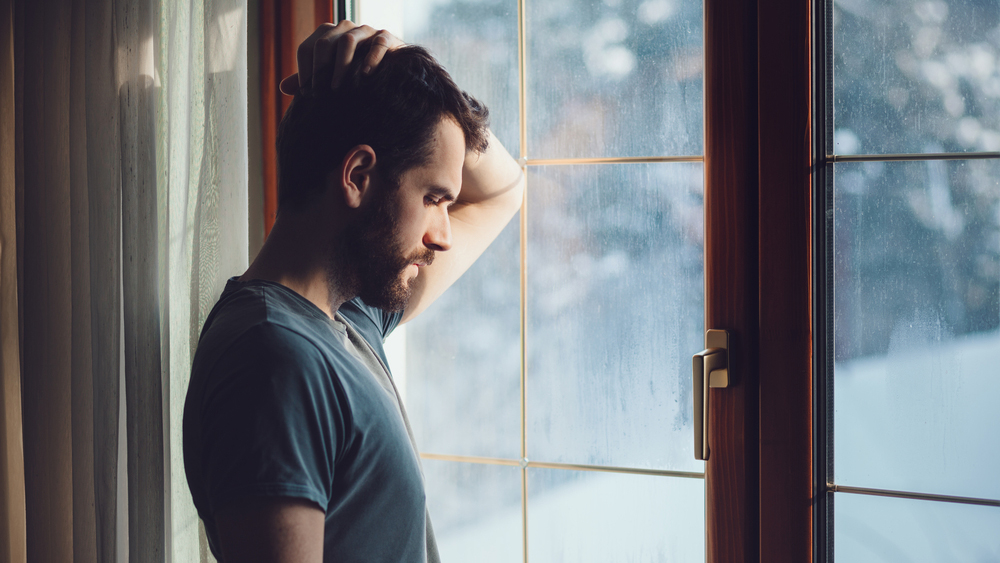 un joven parado junto a una ventana con rayas de lluvia, triste, preocupado, deprimido
