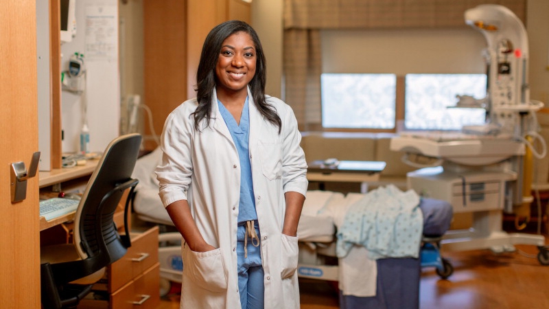 Dr. Kayla Nixon in scrubs and a white jacket smiling in a patient hospital room
