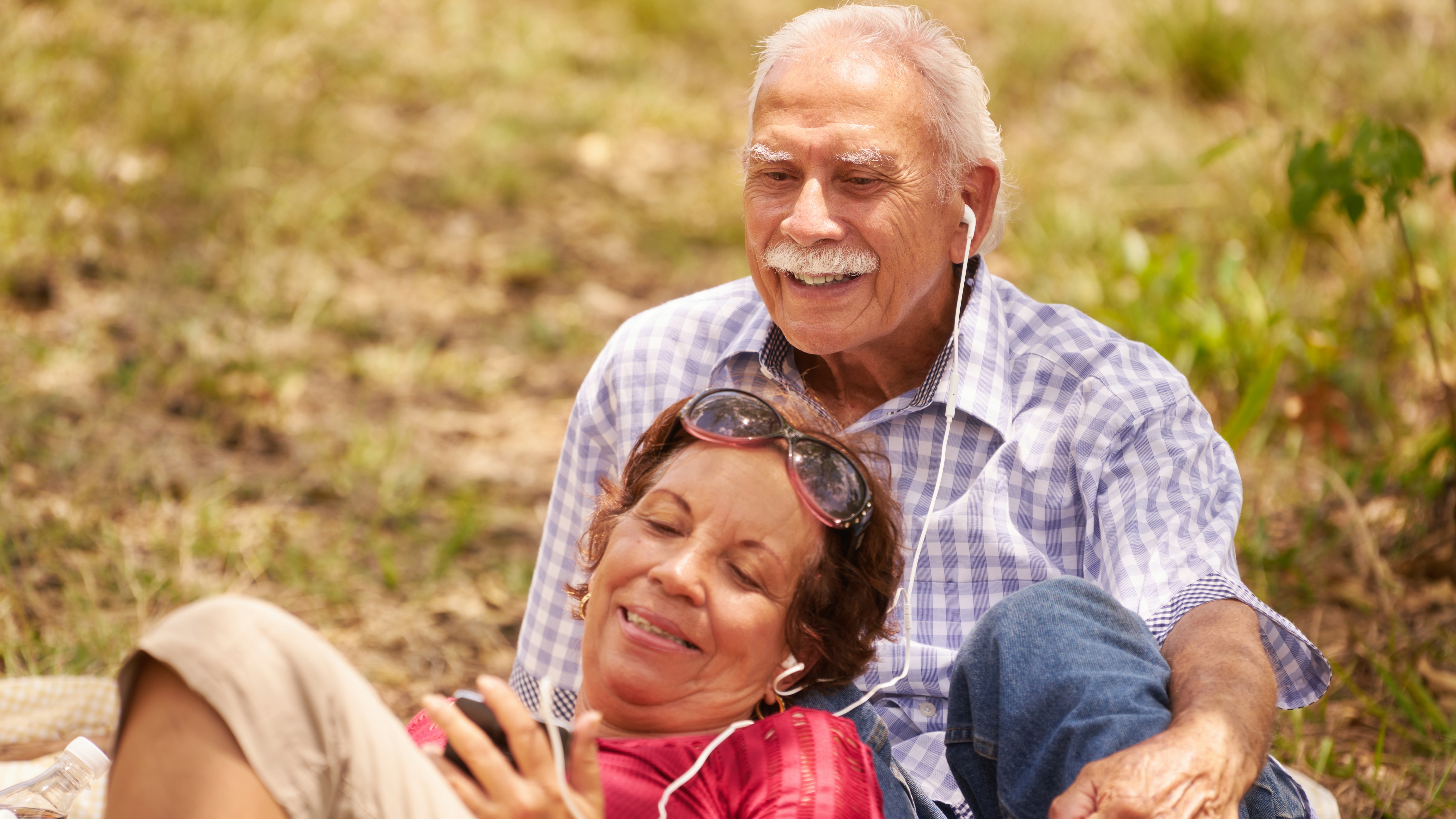 a senior couple, an elderly man and woman in park listening to music with earbuds or headphones