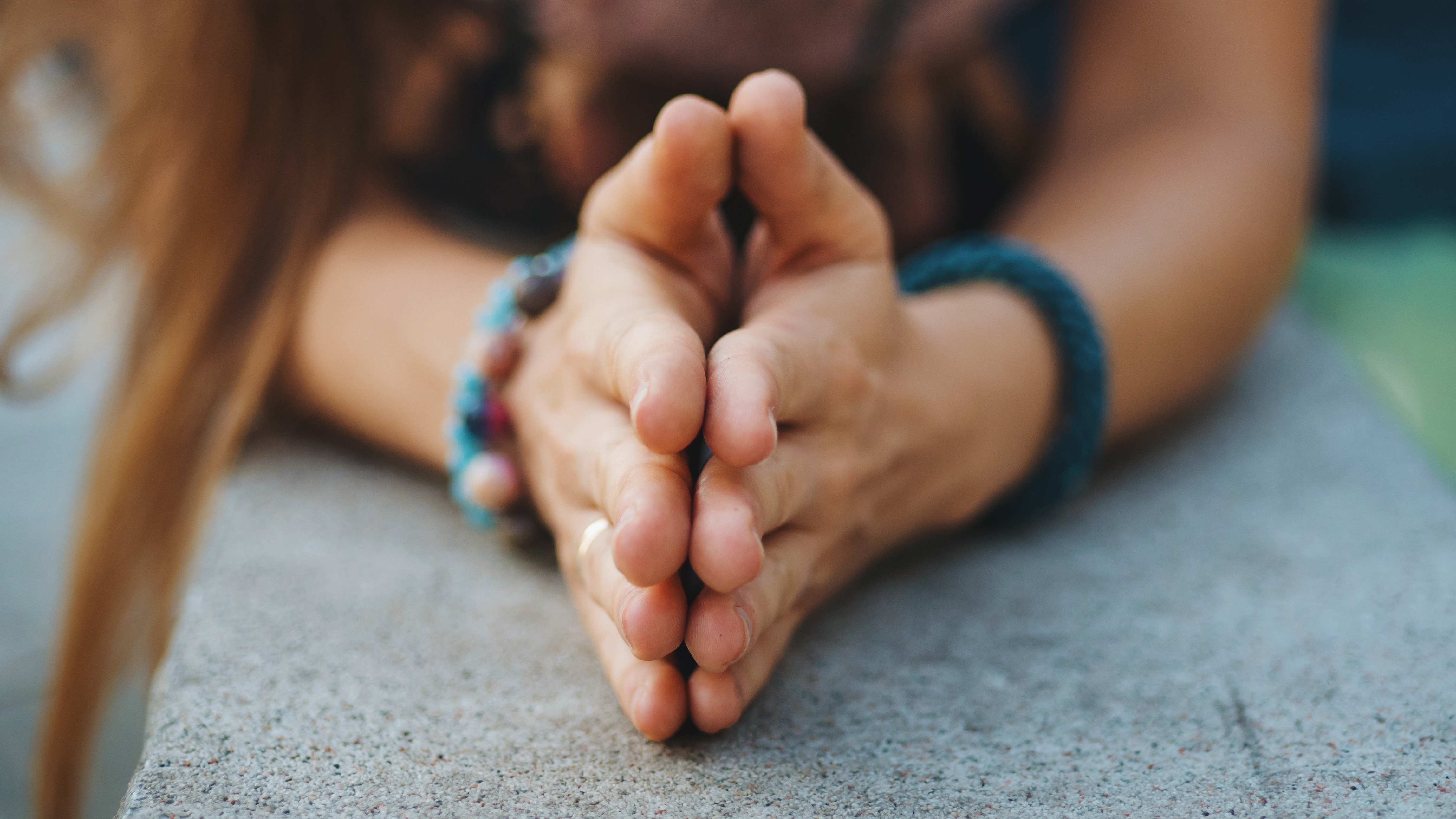 a young women's hands clasped together in a sign of prayer - wearing colorful bracelets