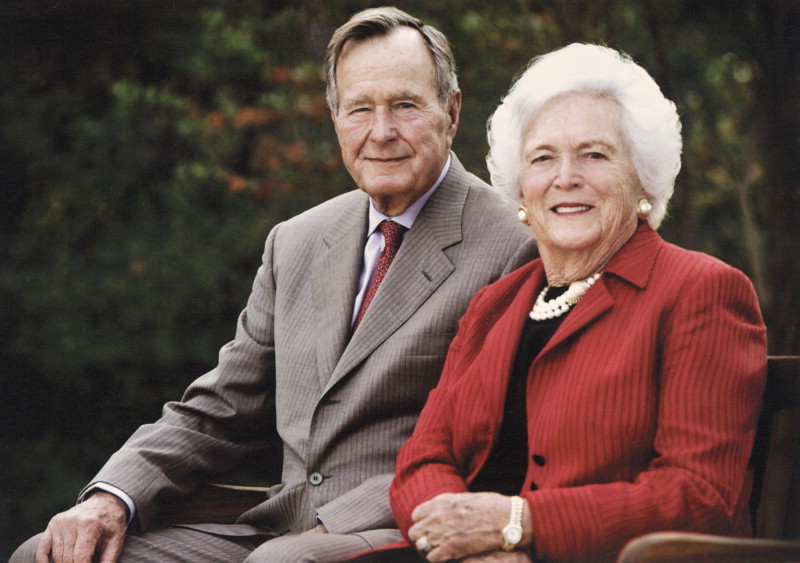 President H.W. Bush and his wife Barbara smiling and sitting outside on a bench