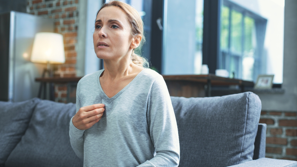 Exhausted mature woman resting on sofa and having hot flash