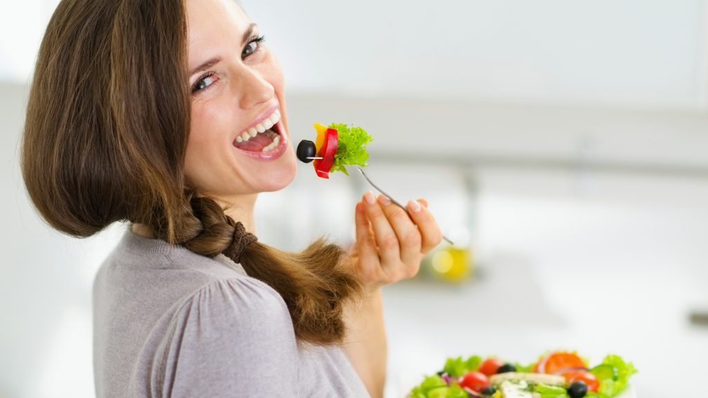 Una mujer sonríe y come una ensalada fresca en una cocina moderna