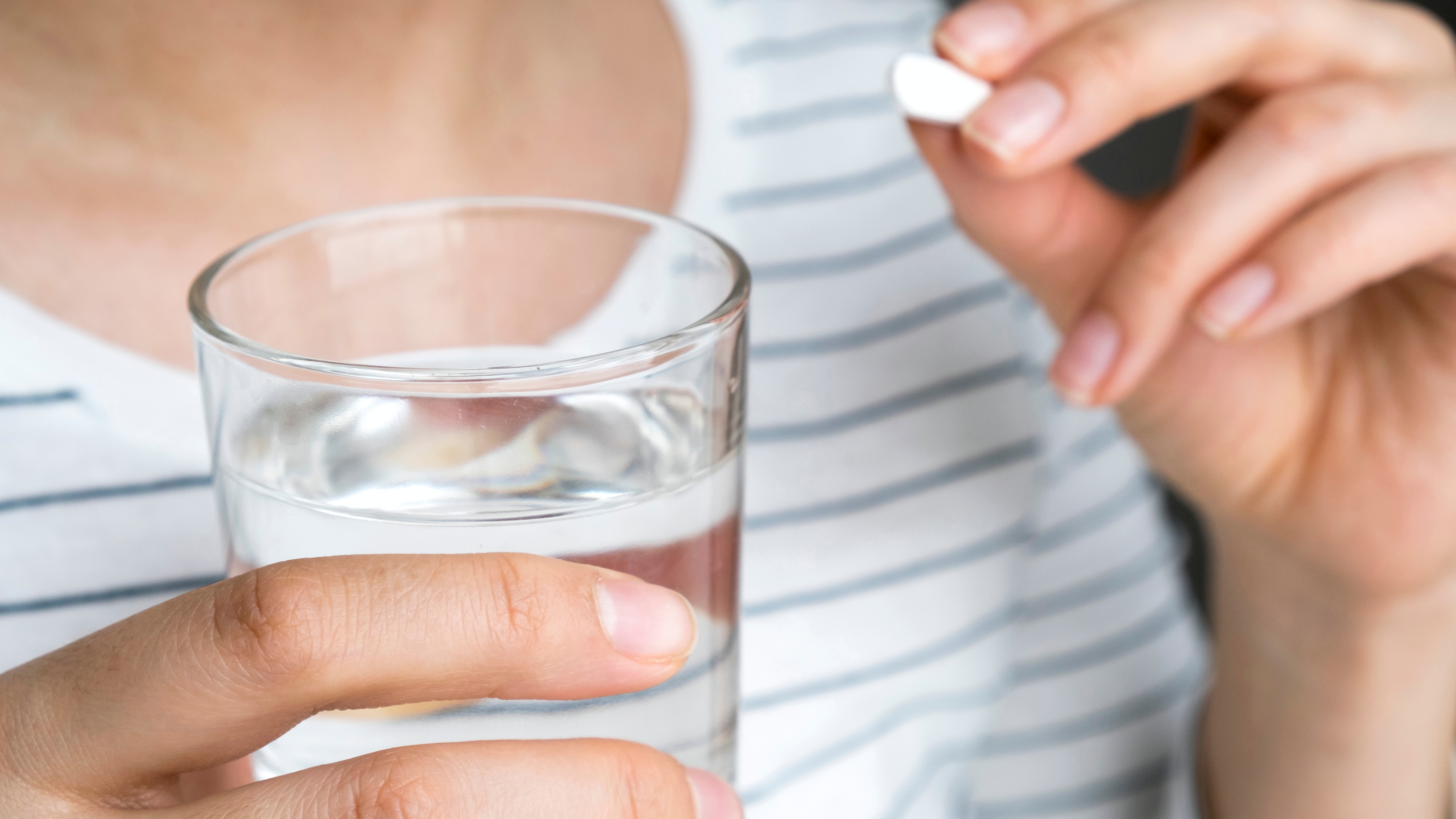 a woman holding a glass of water in one hand an a pill, perhaps prescription medicine, ready to swallow it