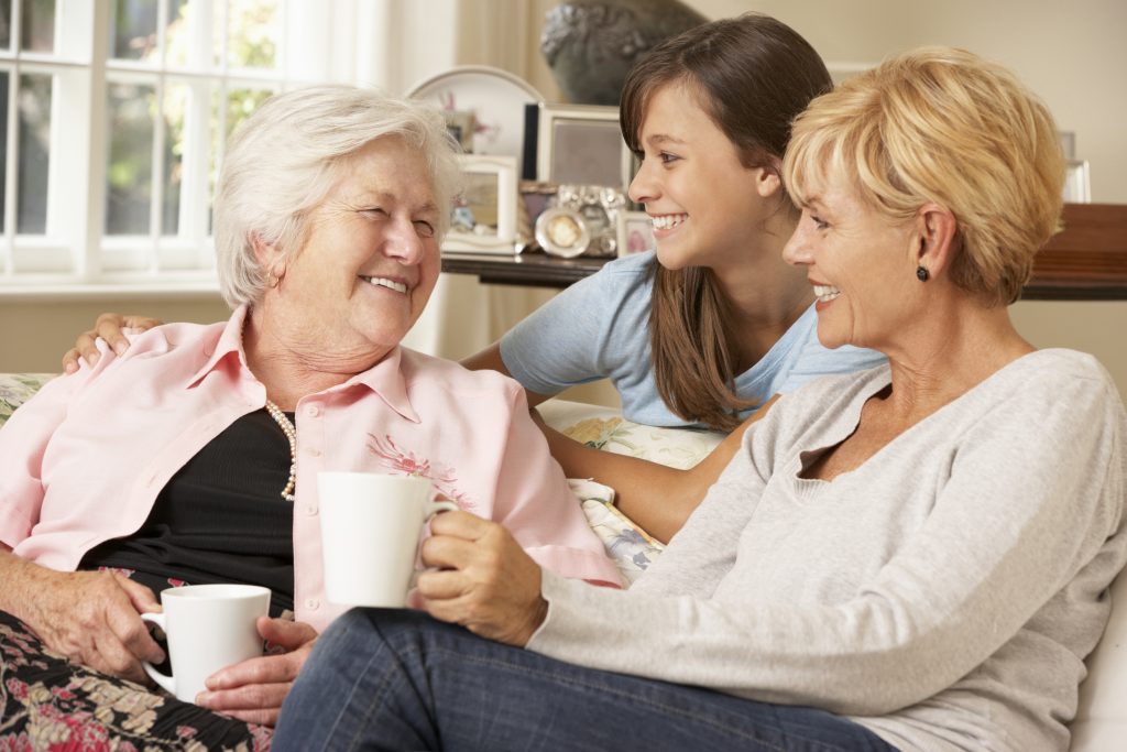 a three generational group of women smiling and having coffee together