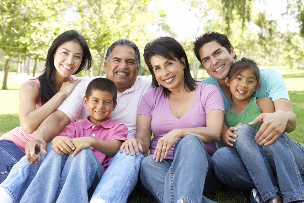 a happy, smiling multi-generational family sitting outside in a park with sunshine and trees