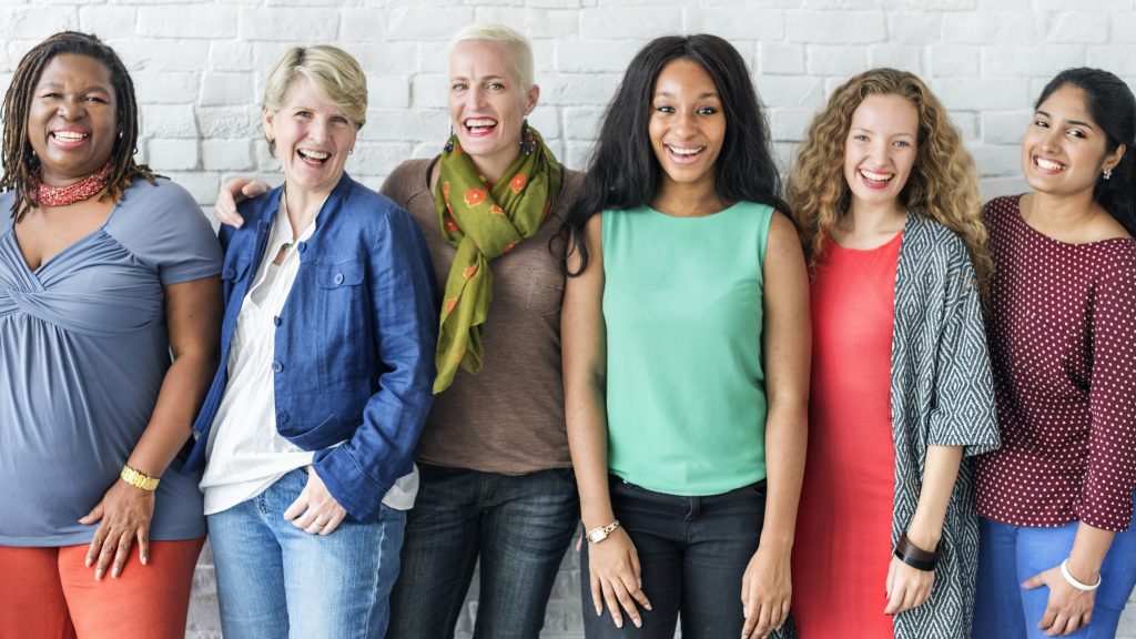 a diverse group of happy, smiling women standing near a brick wall for a background
