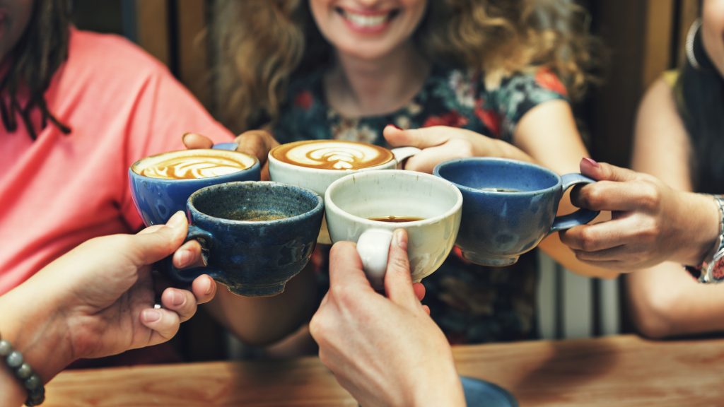 a group of happy diverse women, smiling and sharing cups of coffee together