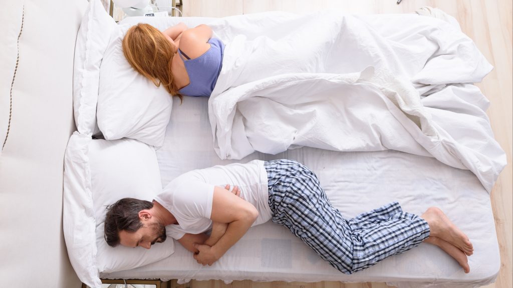 a middle-aged couple in bed with their backs to each other, sleeping or maybe upset, angry, frustrated