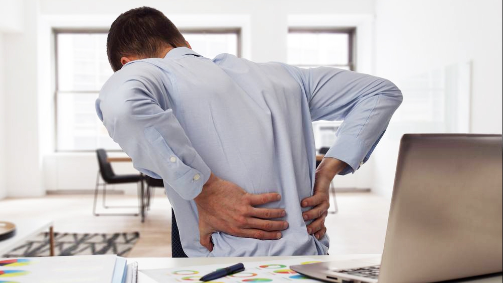 Un ejecutivo sentado en el escritorio con dolor de espalda