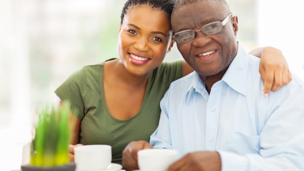 a smiling elderly father and his adult daughter, with cups of tea or coffee
