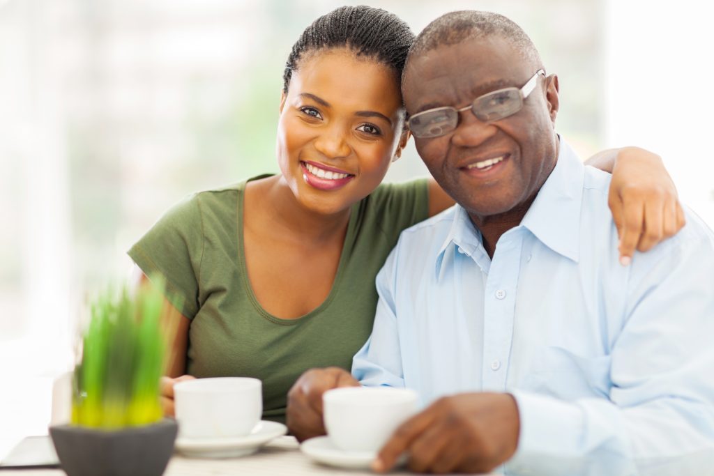 a smiling elderly father and his adult daughter, with cups of tea or coffee