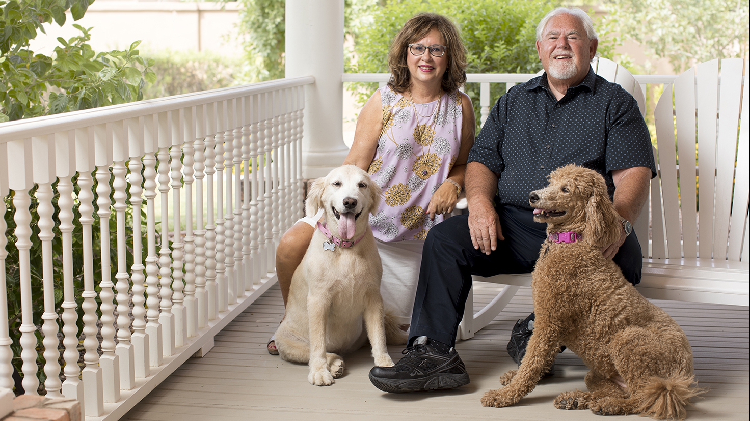 Susan and Tom Gus sitting on a porch with their dogs