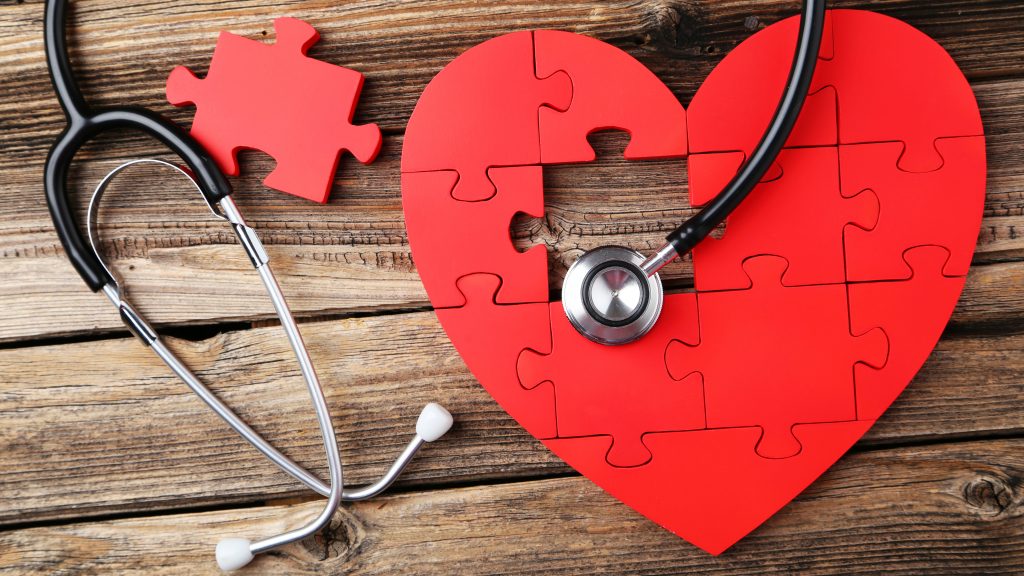 a red heart-shaped puzzle and a stethoscope on a rough wooden surface