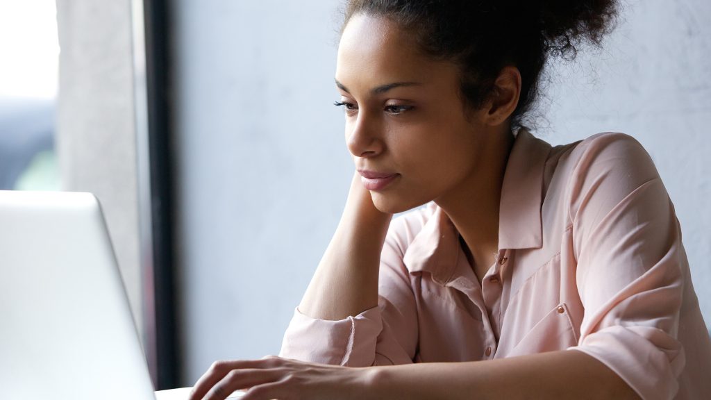 Una joven mujer leyendo información en la pantalla de un portátil, mirando pensativo, serio