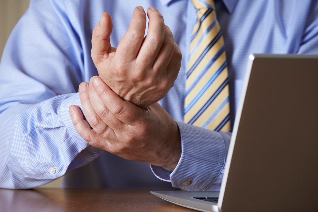 a business man sitting at a computer holding his wrist because of pain and injury