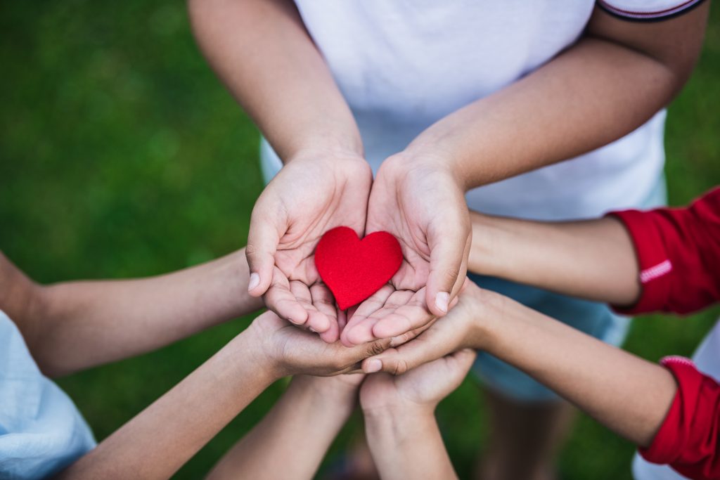 a group of children in a circle with their hands together holding a red paper heart.