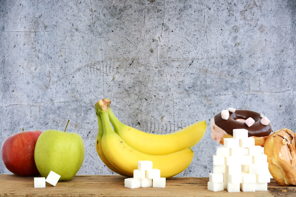 three foods - apples, bananas and pastries - with piles of sugar cubes in front of each, illustrating relative sugar content of each