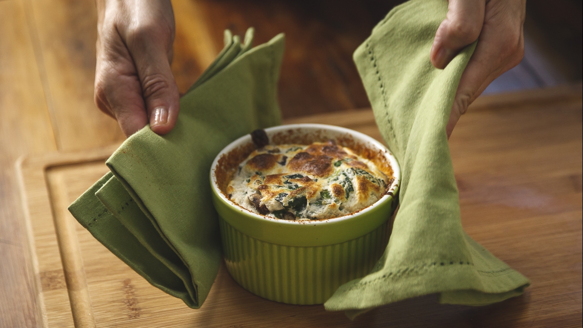 a person holding a dish with napkins - Spinach and mushroom soufflé