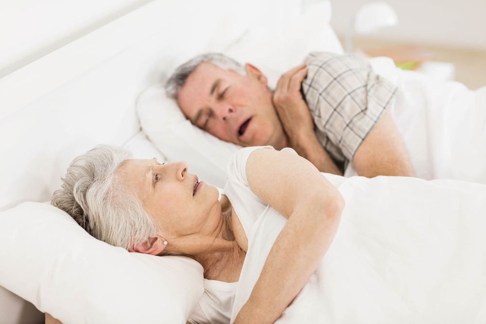 Awake senior woman in bed while her husband is snoring