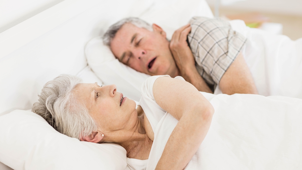Una anciana está despierta en la cama mientras el marido ronca