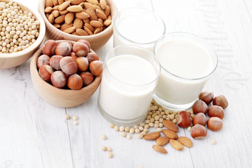 small wooden bowls filled with soybean, almonds and hazelnuts; and three glasses of the corresponding plant milks