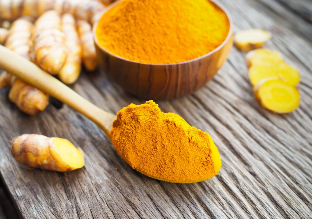 Turmeric powder in wooden spoon on old wooden table.