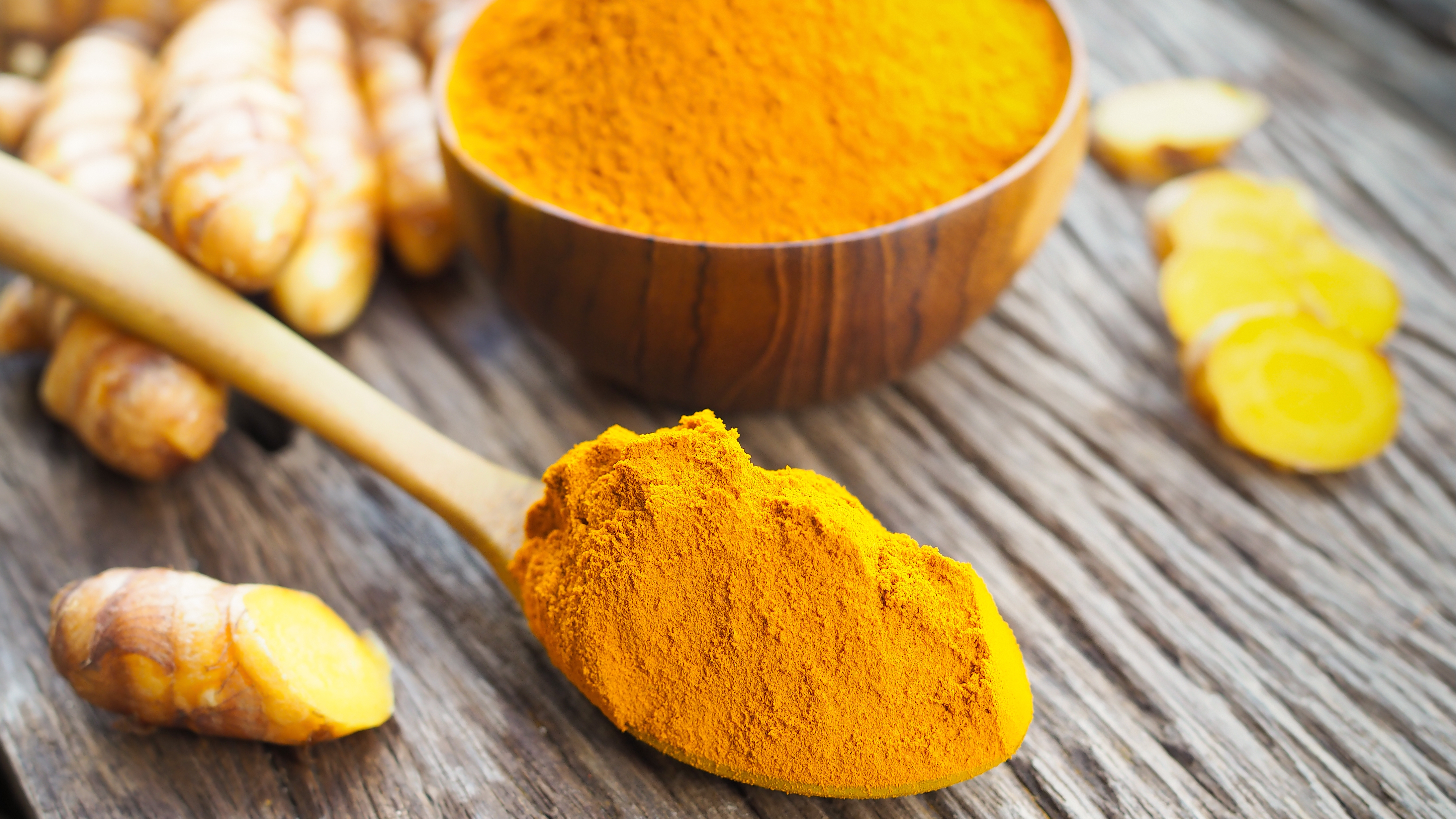 Turmeric powder in wooden spoon on old wooden table.