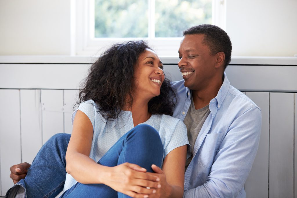an African American woman and man snuggled together at home, looking at one another and smiling