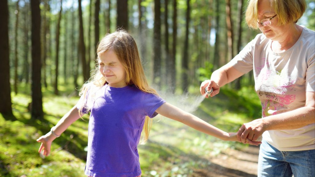 a young girl out in the woods getting tick or bug spray on her arm